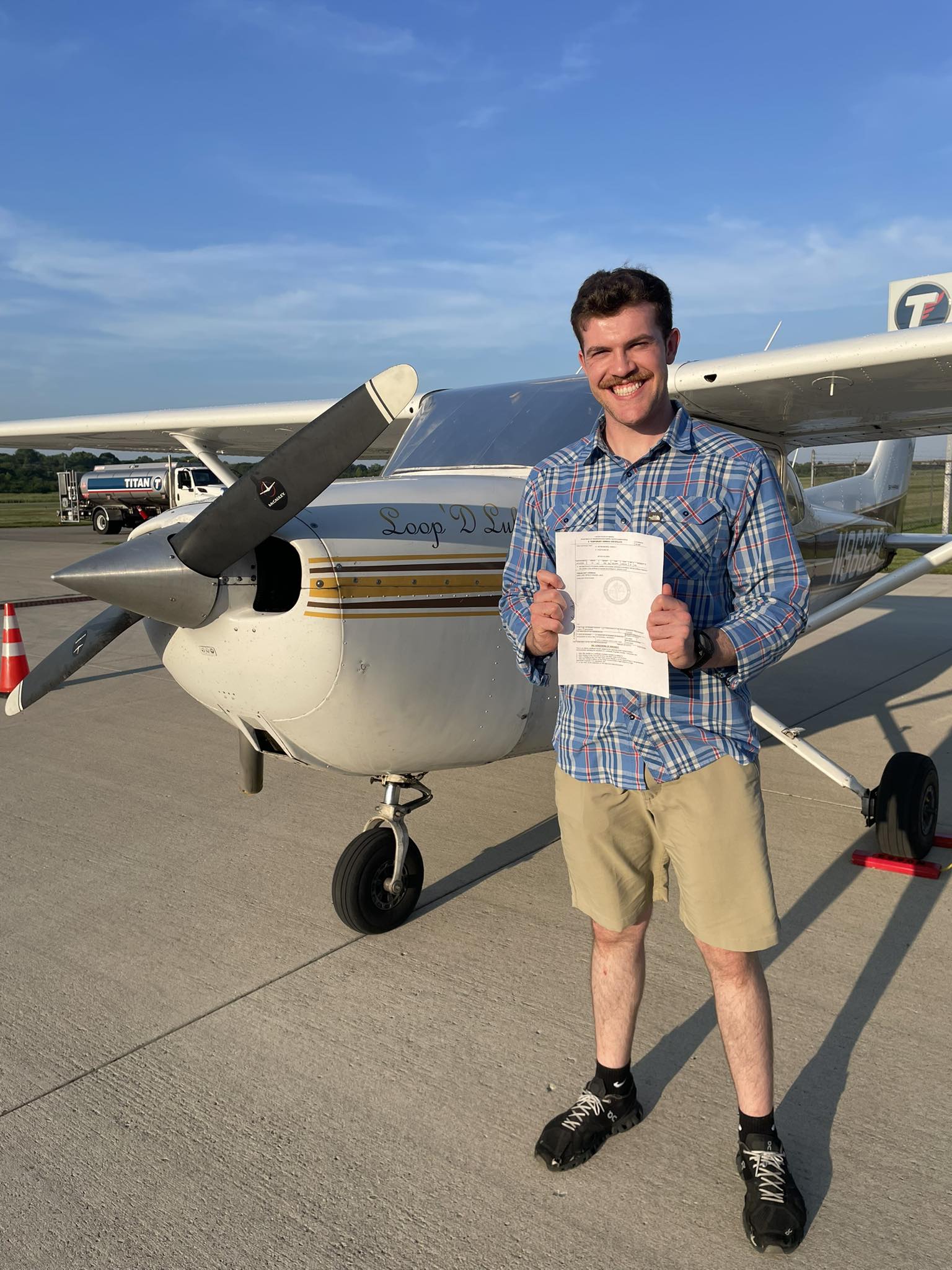 Man smiling and holding certificate in front of an airplane